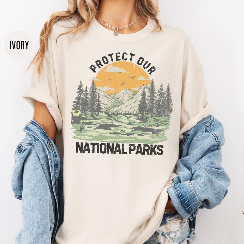 May include: Ivory t-shirt with a vintage-style graphic of a mountain landscape and the text "Protect Our National Parks".