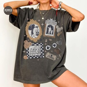 May include: Dark gray t-shirt featuring various cartoon graphics, including Mickey Mouse, cherries, and an ice cream bar. The shirt has a vintage, distressed look with the word "Dream" on a ticket.