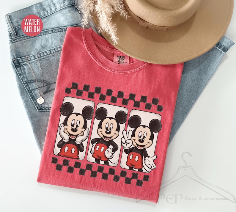 Puede incluir: Una camiseta roja con tres im&aacute;genes de Mickey Mouse en marcos en blanco y negro, sobre un patr&oacute;n de tablero de ajedrez en blanco y negro. La camiseta est&aacute; sobre unos vaqueros azules y un sombrero beige. El texto "WATER MELON" es visible.