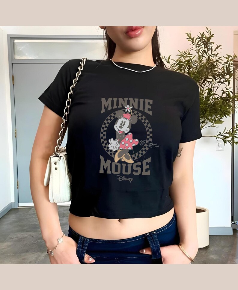 K&ouml;nnte beinhalten: Schwarzes Crop-Top mit Minnie Mouse-Grafik. Das Design zeigt die Worte "MINNIE MOUSE" in einer Vintage-Schrift, mit Minnie Mouse in einem gepunkteten Kleid. Das Disney-Logo ist ebenfalls sichtbar.