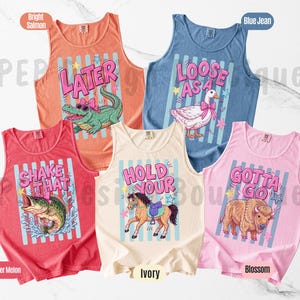 K&ouml;nnte beinhalten: F&uuml;nf &auml;rmellose Tanktops in verschiedenen Farben: helles Lachs, Jeansblau, Wassermelone, Elfenbein und Bl&uuml;ten. Jedes Oberteil hat ein einzigartiges Grafikdesign mit Text und Cartoon-Tieren, darunter ein Alligator, eine Gans, ein Fisch, ein Pferd und ein Bison.