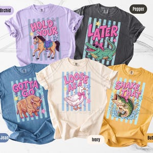 K&ouml;nnte beinhalten: F&uuml;nf farbige T-Shirts mit individuellen Grafiken und Texten. Die Shirts sind in den Farben Orchidee, Pfeffer, Blue Jean, Elfenbein und Butter gehalten. Designs umfassen ein Pferd, Alligator, Bison, Ente und Fisch, mit S&auml;tzen wie "Hold Your", "Later" und "Shake That".