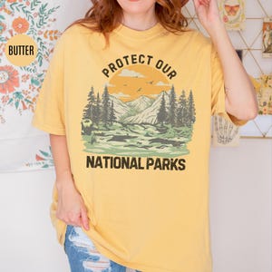 May include: A yellow t-shirt with a vintage-style graphic of a mountain landscape and the text "Protect Our National Parks".