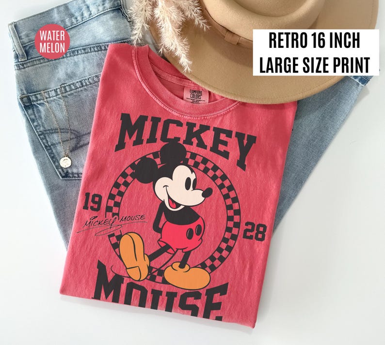 May include: A red t-shirt featuring a graphic of Mickey Mouse. The shirt has the words "Mickey Mouse" in large black letters. The shirt is paired with blue jeans and a tan hat. The text "Retro 16 inch Large Size Print" is visible.