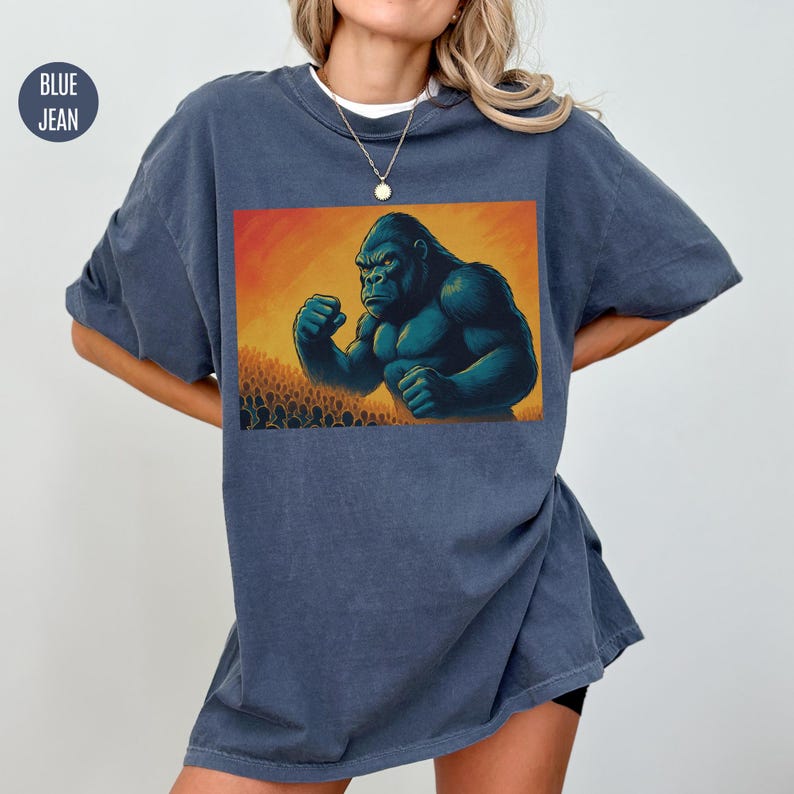 May include: A blue jean oversized t-shirt with a graphic print of a large gorilla standing in front of a crowd of people.