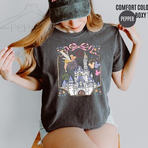 May include: Dark gray Comfort Colors boxy tee featuring a colorful illustration of a fairytale castle, a fairy, fireworks, and Mickey Mouse balloons. The text "COMFORT COLORS" and "BOXY TEE" are printed on the top right.