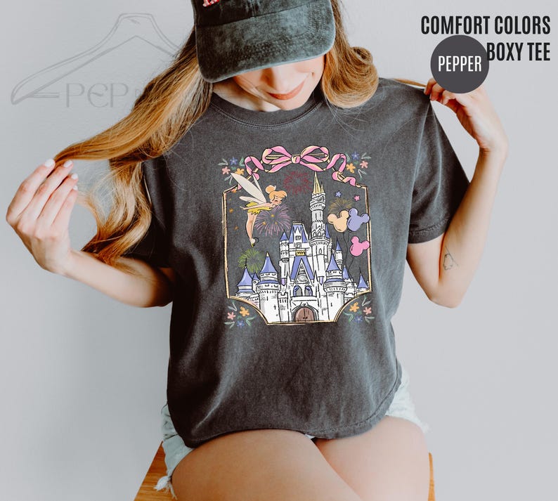 May include: Dark gray Comfort Colors boxy tee featuring a colorful illustration of a fairytale castle, a fairy, fireworks, and Mickey Mouse balloons. The text "COMFORT COLORS" and "BOXY TEE" are printed on the top right.