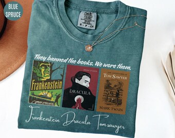 May include: A teal blue t-shirt with a graphic of three classic book covers. The covers are for Frankenstein, Dracula, and The Adventures of Tom Sawyer. The text "They banned the books. We wore them." is printed above the covers. The text "Frankenstein Dracula Tom Sawyer" is printed below the covers.
