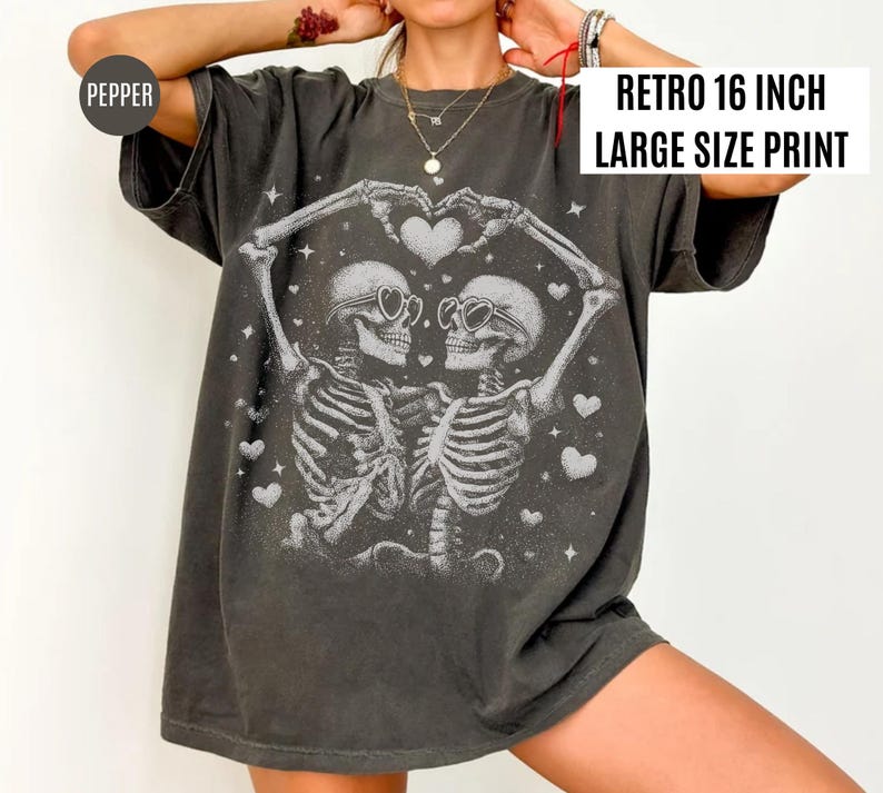 May include: Dark gray t-shirt with a large print featuring two skeletons embracing, forming a heart shape with their arms. The skeletons wear sunglasses and are surrounded by hearts and stars. The text "RETRO 16 INCH LARGE SIZE PRINT" is displayed on the upper right.