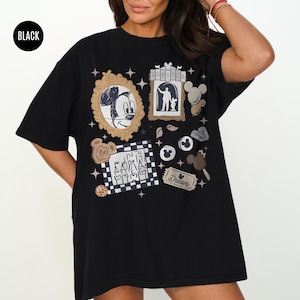 May include: Black t-shirt featuring various Disney-themed graphics, including Mickey Mouse, a silhouette, and other cartoon elements. The shirt has a round neckline and short sleeves. The word "Dream" is also visible on the shirt.