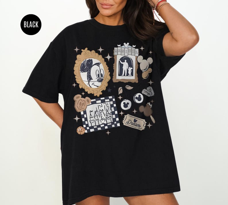 May include: Black t-shirt featuring various Disney-themed graphics, including Mickey Mouse, a silhouette, and other cartoon elements. The shirt has a round neckline and short sleeves. The word "Dream" is also visible on the shirt.