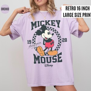 May include: Orchid-colored oversized t-shirt featuring a large graphic of Mickey Mouse. The design includes the text "Mickey Mouse" and "Disney" in dark green, with the year "1928". The shirt has a "Retro 16 inch Large Size Print" label.