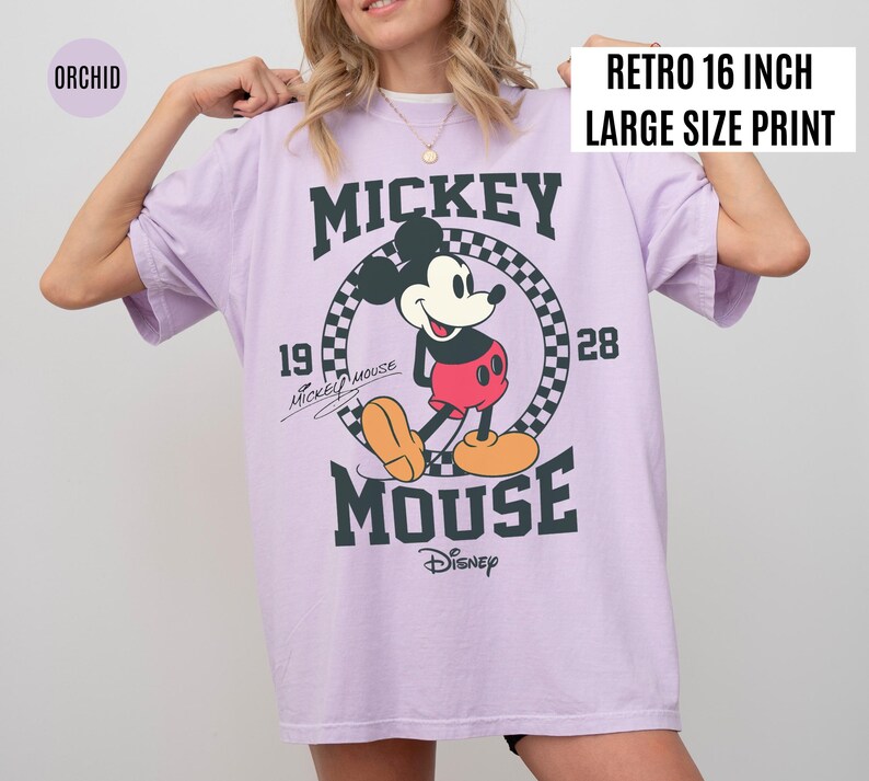May include: Orchid-colored oversized t-shirt featuring a large graphic of Mickey Mouse. The design includes the text "Mickey Mouse" and "Disney" in dark green, with the year "1928". The shirt has a "Retro 16 inch Large Size Print" label.