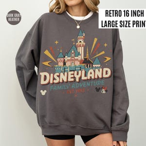 May include: Dark gray heather sweatshirt with a retro Disneyland graphic. The design features a castle, stars, and the text "Disneyland Family Adventure Est. 1955". The print is 16 inches in size.