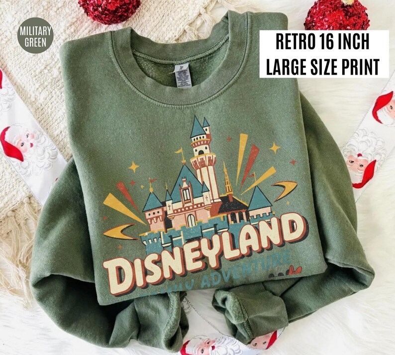 May include: Military green sweatshirt with a retro Disneyland castle graphic. The design includes the text "Disneyland" in a vintage font, with a large size print.