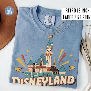Puede incluir: Camiseta azul vaquero con un gr&aacute;fico retro del castillo de Disneyland. El gr&aacute;fico utiliza tonos rojos, naranjas, verdes y amarillos. El texto "DISNEYLAND" est&aacute; impreso en la parte inferior. La camiseta tiene una etiqueta "Comfort Colors". La impresi&oacute;n mide 40,6 cm de ancho.