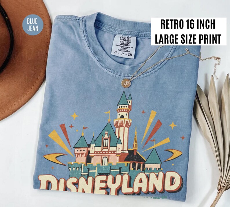 Puede incluir: Camiseta azul vaquero con un gr&aacute;fico retro del castillo de Disneyland. El gr&aacute;fico utiliza tonos rojos, naranjas, verdes y amarillos. El texto "DISNEYLAND" est&aacute; impreso en la parte inferior. La camiseta tiene una etiqueta "Comfort Colors". La impresi&oacute;n mide 40,6 cm de ancho.