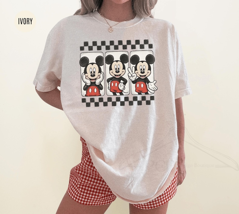 Puede incluir: Camiseta de color marfil con un gr&aacute;fico de Mickey Mouse en tres poses diferentes, sobre un fondo a cuadros blanco y negro. Mickey lleva pantalones cortos rojos y guantes blancos. La camiseta se combina con pantalones cortos a cuadros rojos y blancos.