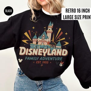May include: Black sweatshirt with a retro Disneyland graphic. The design features a castle, the word "Disneyland", and the text "Family Adventure + EST. 1955 +." The sweatshirt has the text "RETRO 16 INCH LARGE SIZE PRINT" and the word "BLACK" on it.