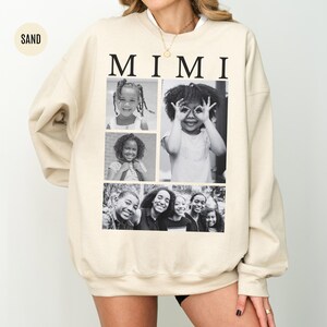 May include: A sand-coloured sweatshirt with the word "MIMI" in black capital letters. The sweatshirt displays a collage of black and white photographs of children. The style of the sweatshirt is casual and comfortable.