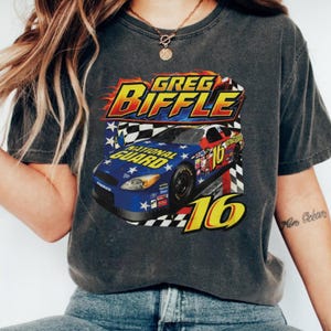 May include: Dark grey t-shirt with a racing car graphic. The design includes the text "GREG BIFFLE" and "NATIONAL GUARD", with a blue, red, and white car bearing the number 16. Flames and a chequered flag are also present.