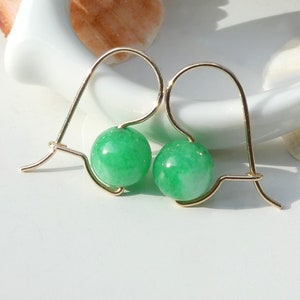 May include: A pair of gold hoop earrings with green jade stone beads. The earrings are simple and elegant.