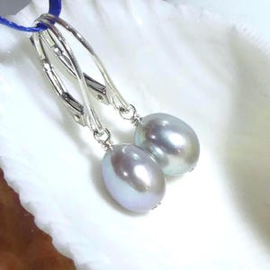 May include: A pair of drop earrings featuring oval-shaped, iridescent light gray pearls suspended from polished silver-tone leverback hooks. The pearls exhibit a smooth, lustrous surface with subtle hints of blue and purple undertones in the light.