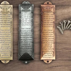 May include: Three mezuzahs with Hebrew text and English translations. The mezuzahs are made of metal and have a traditional design. The mezuzahs are in gold, silver, and bronze.