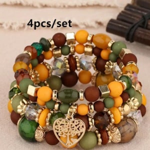 May include: Set of four bracelets with brown, yellow, green, and gold beads. The bracelets are stacked on top of each other and feature a gold heart charm with a tree design. The text "4pcs/set" is visible in the image.