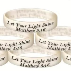 May include: Six white silicone wristbands stacked on top of each other. Each band has the text "Let Your Light Shine Matthew 5:16" printed in black. The bands are circular and have a slightly translucent appearance.