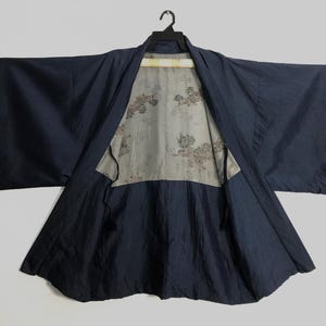 May include: Navy blue kimono jacket with a floral patterned lining. The jacket is open, revealing the interior design. The sleeves are wide and the fabric has a slight sheen. The garment is hanging on a black hanger.