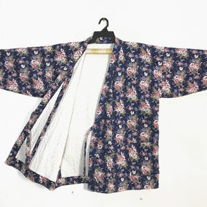 May include: A navy blue floral kimono jacket with a white quilted lining. The jacket features a pattern of pink, white, and purple flowers. It is hanging on a black hanger against a white background.