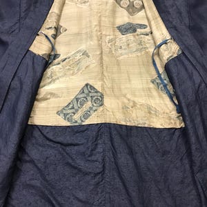 Puede incluir: Un kimono azul marino con un interior estampado. El forro interior es de color beige claro con patrones rectangulares azules y grises. El kimono est&aacute; abierto, revelando el dise&ntilde;o interior. La tela exterior tiene una apariencia sutilmente texturizada.