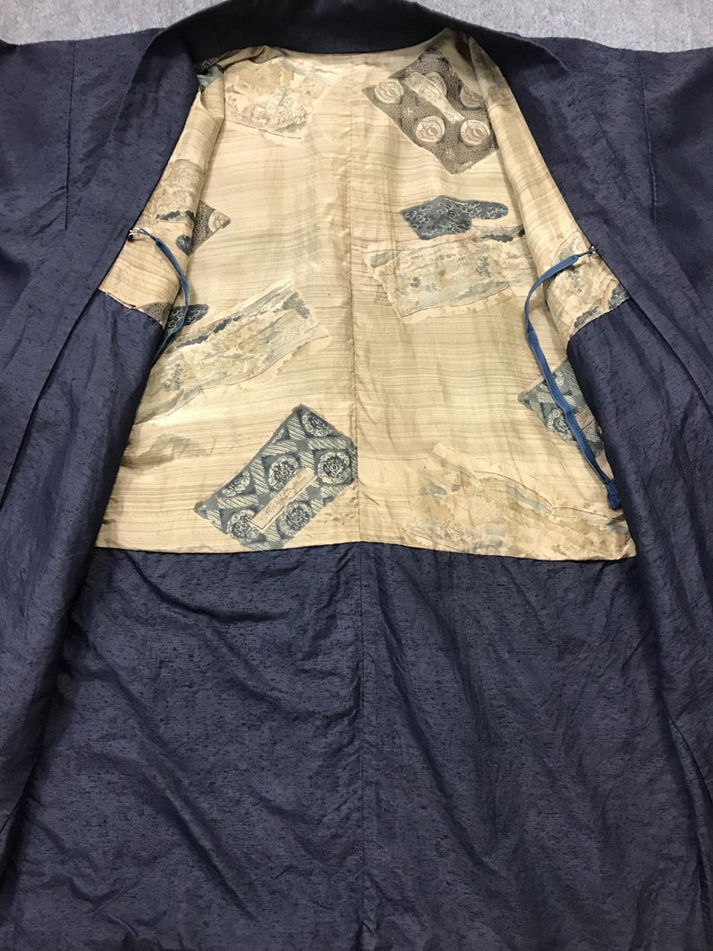 Puede incluir: Un kimono azul marino con un interior estampado. El forro interior es de color beige claro con patrones rectangulares azules y grises. El kimono est&aacute; abierto, revelando el dise&ntilde;o interior. La tela exterior tiene una apariencia sutilmente texturizada.