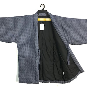 May include: A blue and gray patterned kimono-style jacket with a black interior. The jacket is hanging on a black hanger against a white background. The pattern consists of vertical lines with small circular designs.