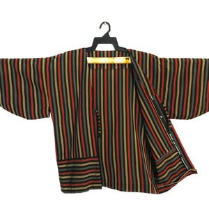 May include: A short-sleeved kimono-style jacket featuring a vertical striped pattern in shades of black, red, and tan. The garment is displayed on a black plastic hanger and includes a small white label on the inner lining with text.