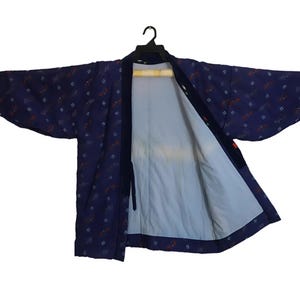 Puede incluir: Una chaqueta azul oscuro estilo kimono con un estampado floral en rojo y blanco. La chaqueta está abierta, revelando un interior azul claro. La prenda está colgada de una percha negra sobre un fondo blanco.