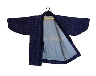 Puede incluir: Una chaqueta azul oscuro estilo kimono con un estampado floral en rojo y blanco. La chaqueta está abierta, revelando un interior azul claro. La prenda está colgada de una percha negra sobre un fondo blanco.