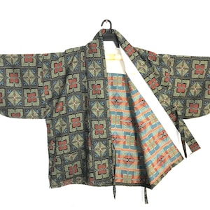 May include: A haori jacket featuring a dark green exterior with a repeating geometric floral pattern in red, blue, and gold. The interior lining displays a contrasting light blue and orange geometric print with thin ties at the front opening.