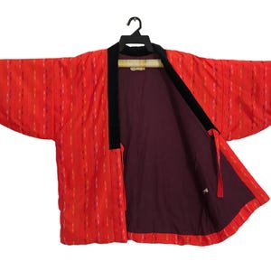 Puede incluir: Un kimono de estilo japonés rojo y negro con un patrón geométrico. El kimono está abierto y el forro es de color burdeos oscuro.