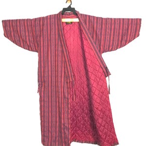 May include: A red and purple striped kimono-style robe with a quilted interior. The robe is hanging on a black hanger. The robe has long sleeves and a tie closure.