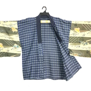 May include: A blue and white plaid kimono-style jacket with wide sleeves. The sleeves feature a patterned design with yellow and green accents. The jacket is open in the front and hangs from a black hanger.
