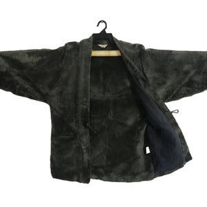 Puede incluir: Chaqueta texturizada gris oscuro con frente abierto y mangas largas. La chaqueta está colgada de una percha negra. El forro interior es de un tono gris más oscuro. La chaqueta tiene un cierre de lazo.