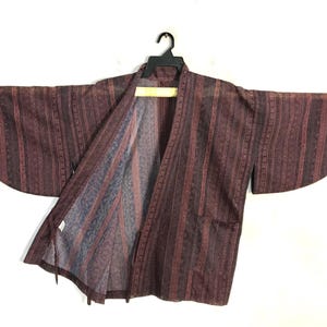 May include: A dark maroon and black striped haori jacket featuring wide sleeves and an open front design. The fabric displays a repeating geometric pattern within the vertical stripes, with a visible inner lining showing a lighter blue and grey tone.