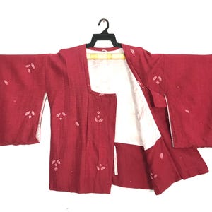 May include: A deep red haori jacket featuring a subtle white leaf pattern scattered across the fabric. The garment has wide sleeves, an open front, and a contrasting white lining visible on the interior panels and along the front edges.