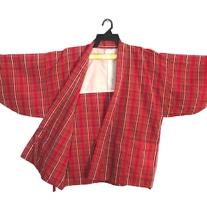 May include: A red plaid haori jacket featuring a pattern of thin white and dark lines. The garment has wide, loose sleeves, an open front design, and a white inner lining visible at the collar. It is displayed on a black plastic clothes hanger.