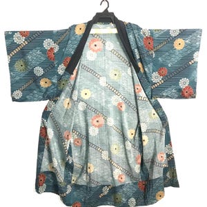 May include: A teal kimono featuring a repeating pattern of white, yellow, and red chrysanthemum flowers, diagonal chains, and wave motifs. The garment has wide sleeves, a solid black collar, and a lighter teal interior lining with matching floral prints.