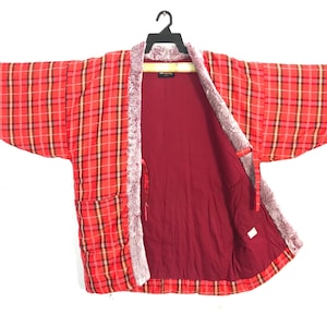 May include: Red plaid kimono-style jacket with a faux fur trim and a burgundy interior. The jacket is hanging on a black hanger against a white background. The plaid pattern includes red, black, and yellow lines.