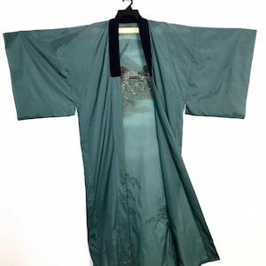Puede incluir: Kimono de color verde azulado con cuello negro y diseño de paisaje en el interior. El kimono está colgado de una percha negra sobre un fondo blanco. El diseño del paisaje presenta una escena de montaña y edificio.