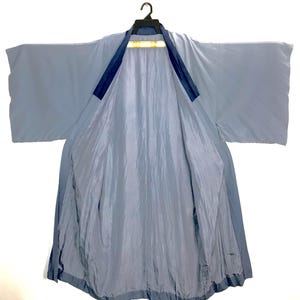 May include: A light blue kimono with wide sleeves and a darker blue collar trim. The garment is open at the front, revealing a matching light blue lining. It is displayed on a black hanger against a plain white background, showing a smooth texture.